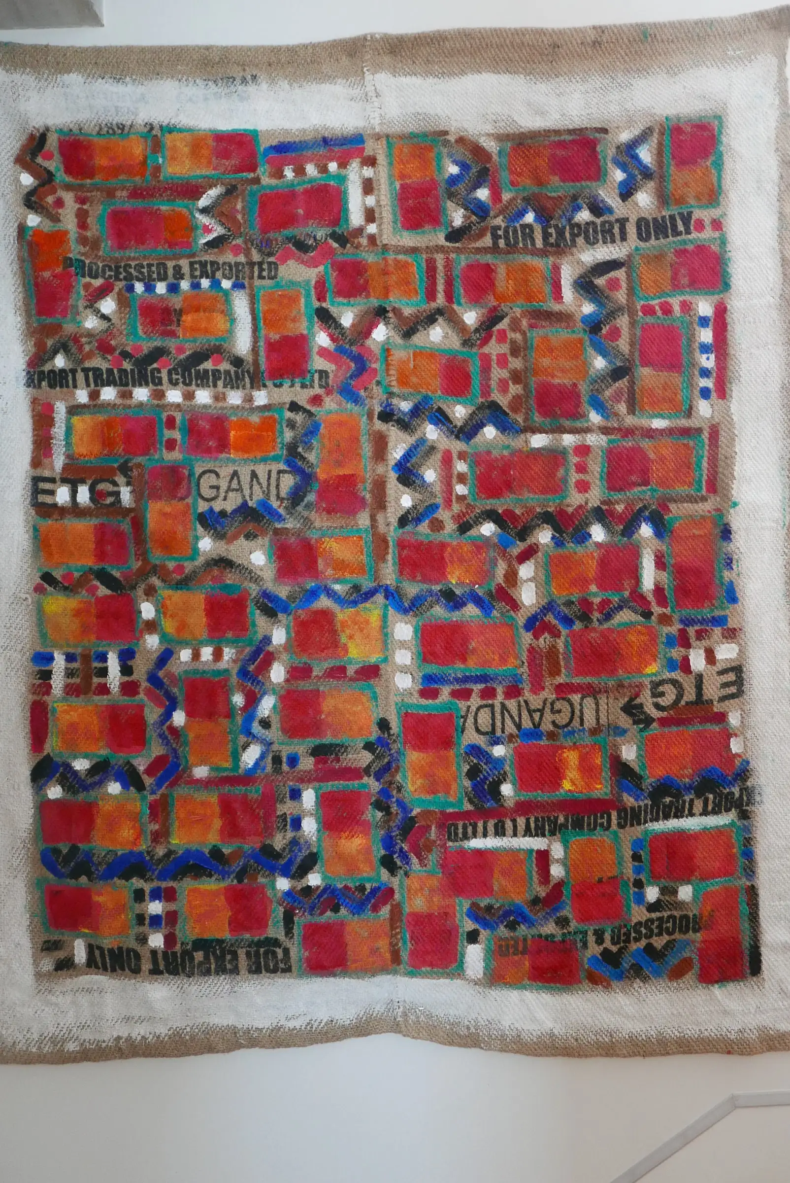 Africano, de la serie Arpilleras: retícula de rectángulos rojos y naranjas sobre saco de yute con la inscripción For export only
